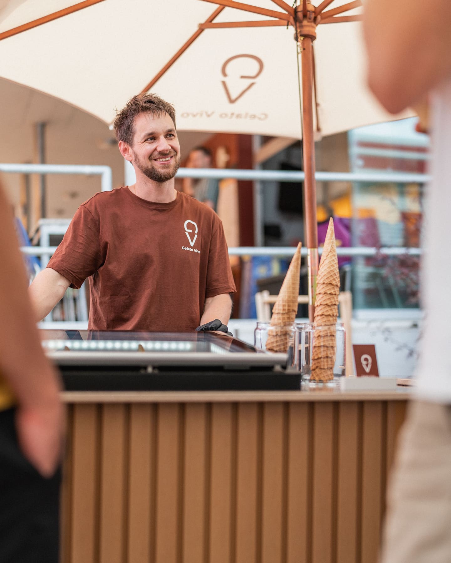 Stefan von Gelato Vivo lächelt hinter der mobilen Gelato Bar mit Cornets und Sonnenschirm